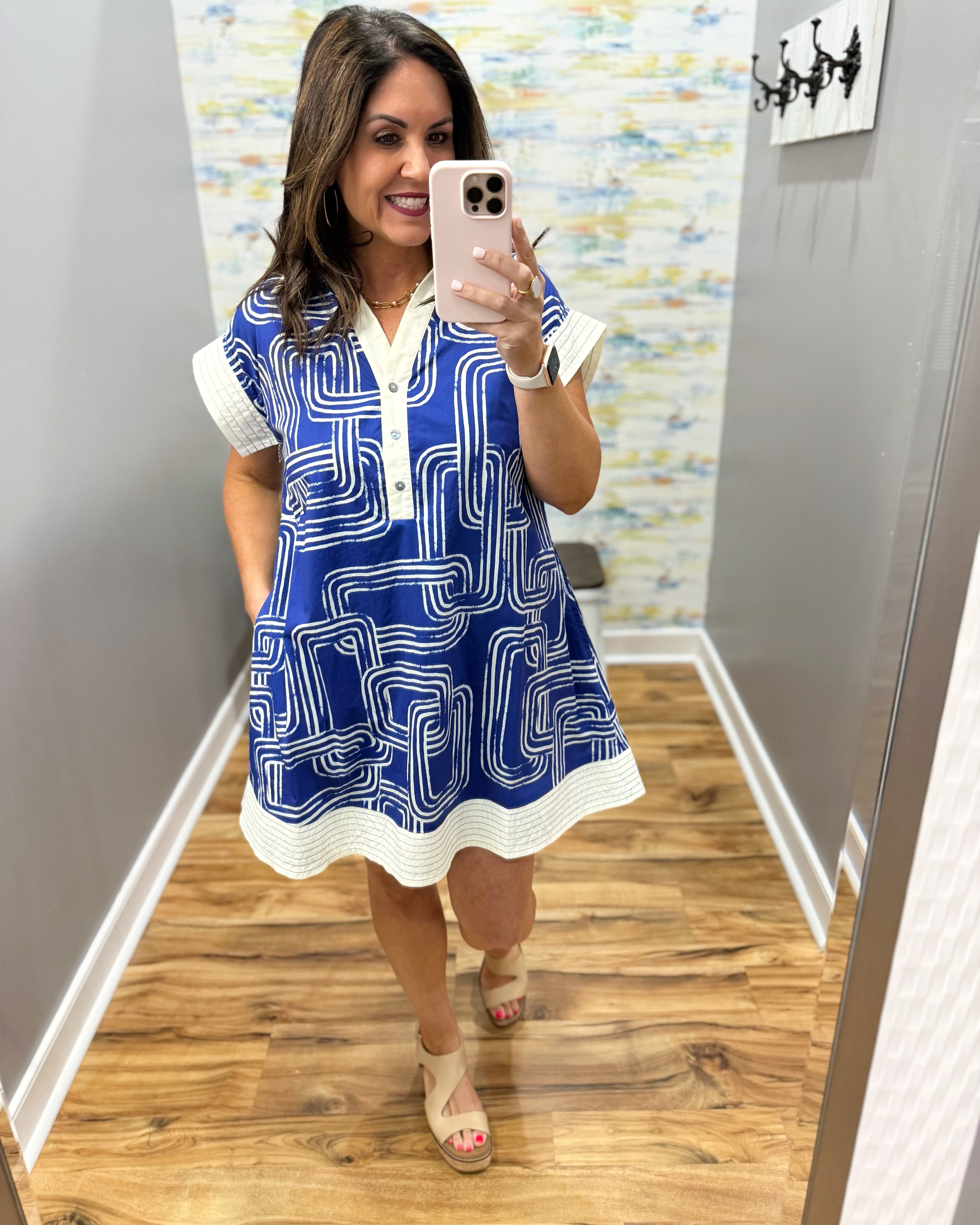 Woman taking a mirror selfie wearing a blue and white dress with a geometric pattern.