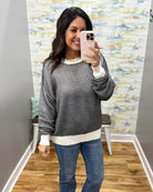A woman takes a mirror selfie wearing a gray and white horizontally striped long-sleeve sweater with a cream ribbed hem and cuffs, paired with blue jeans.
