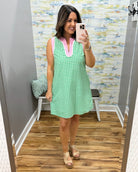 Woman taking a mirror selfie wearing a green checkered dress with pink trim.