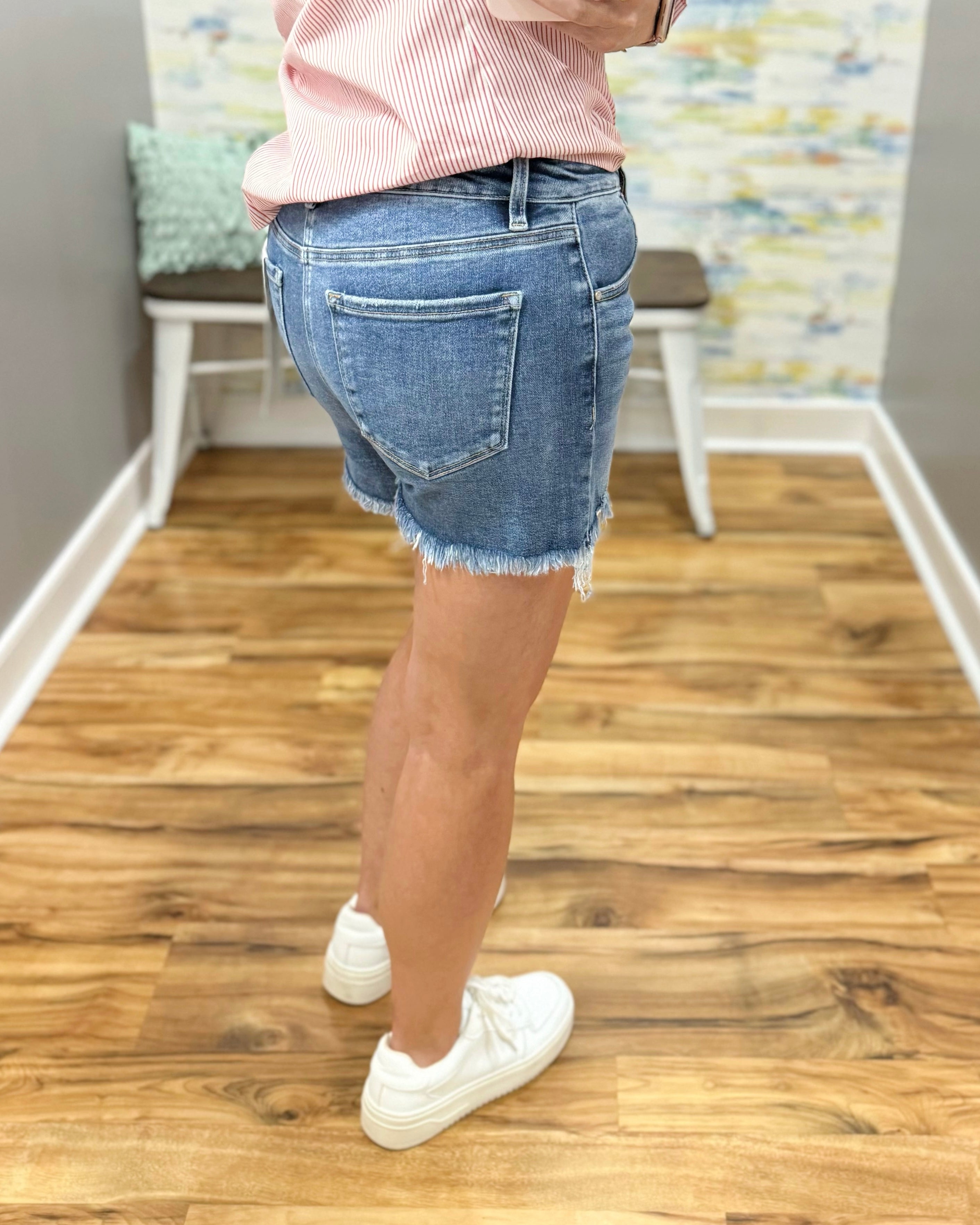 Person wearing blue denim shorts and a pink shirt in a room with wooden flooring.