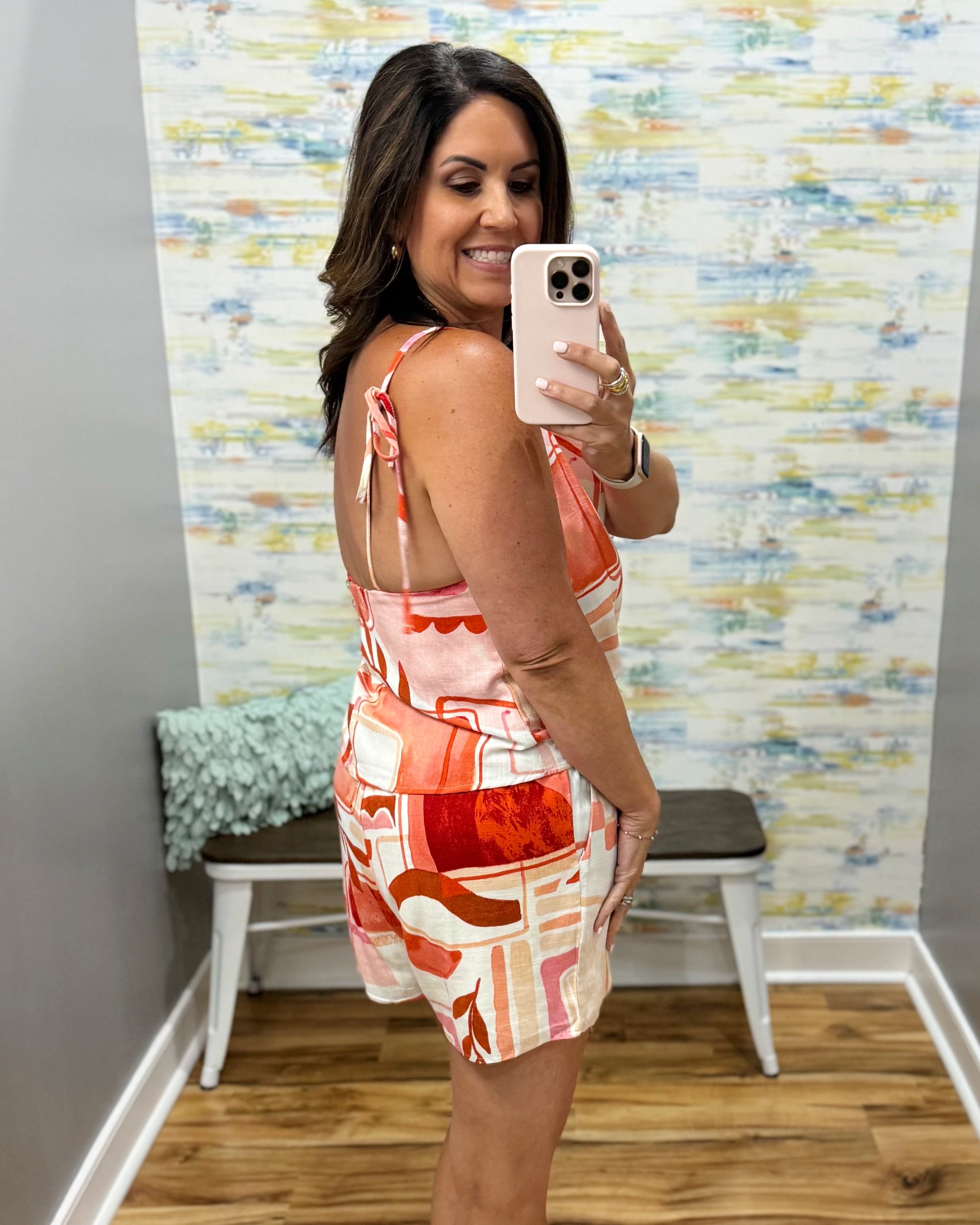 Woman taking a mirror selfie wearing a colorful dress in a room with a patterned wall.