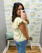 Woman taking a mirror selfie wearing a floral blouse and blue jeans in a room with colorful wall art.