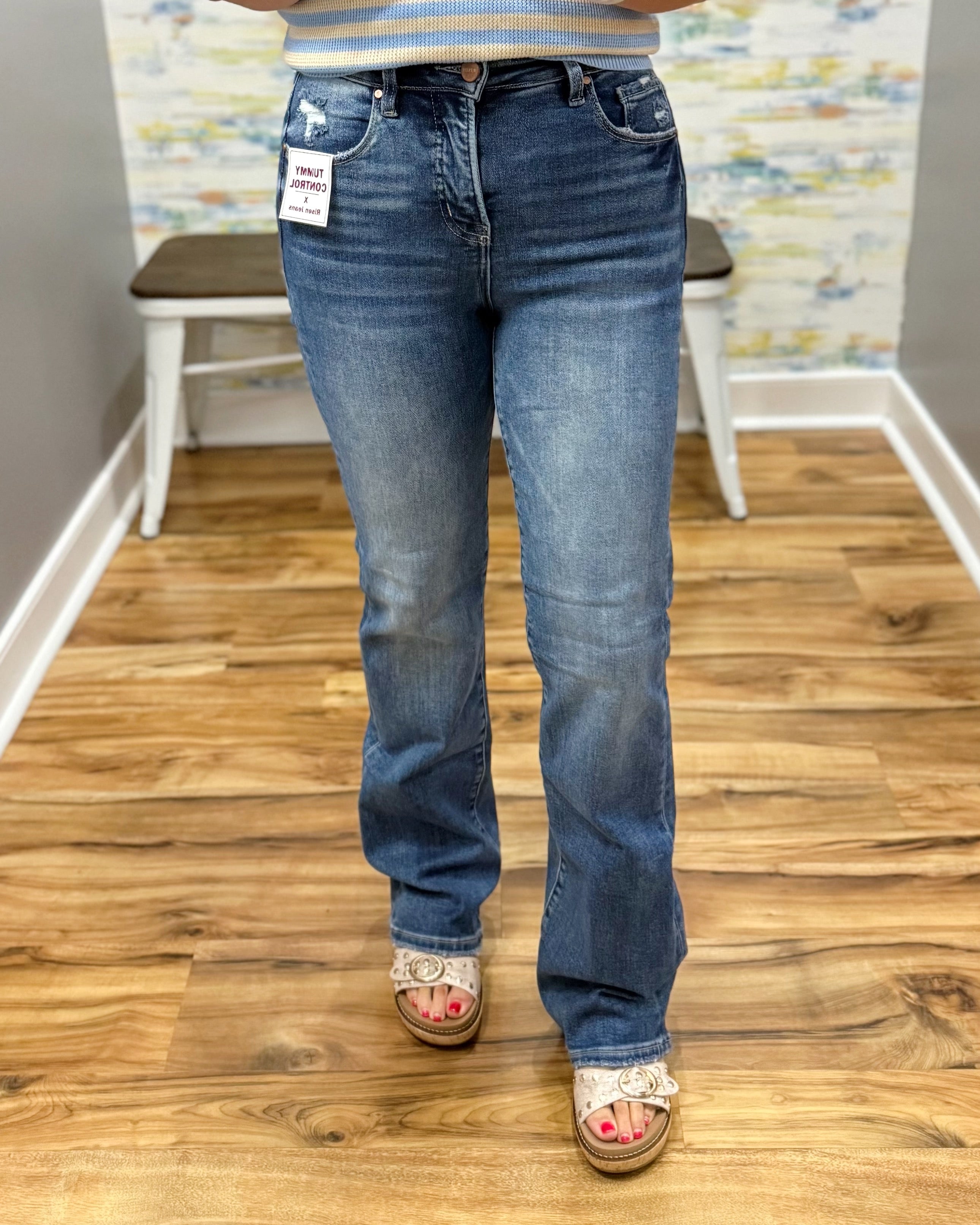 Person wearing blue jeans with a tag, standing on a wooden floor.