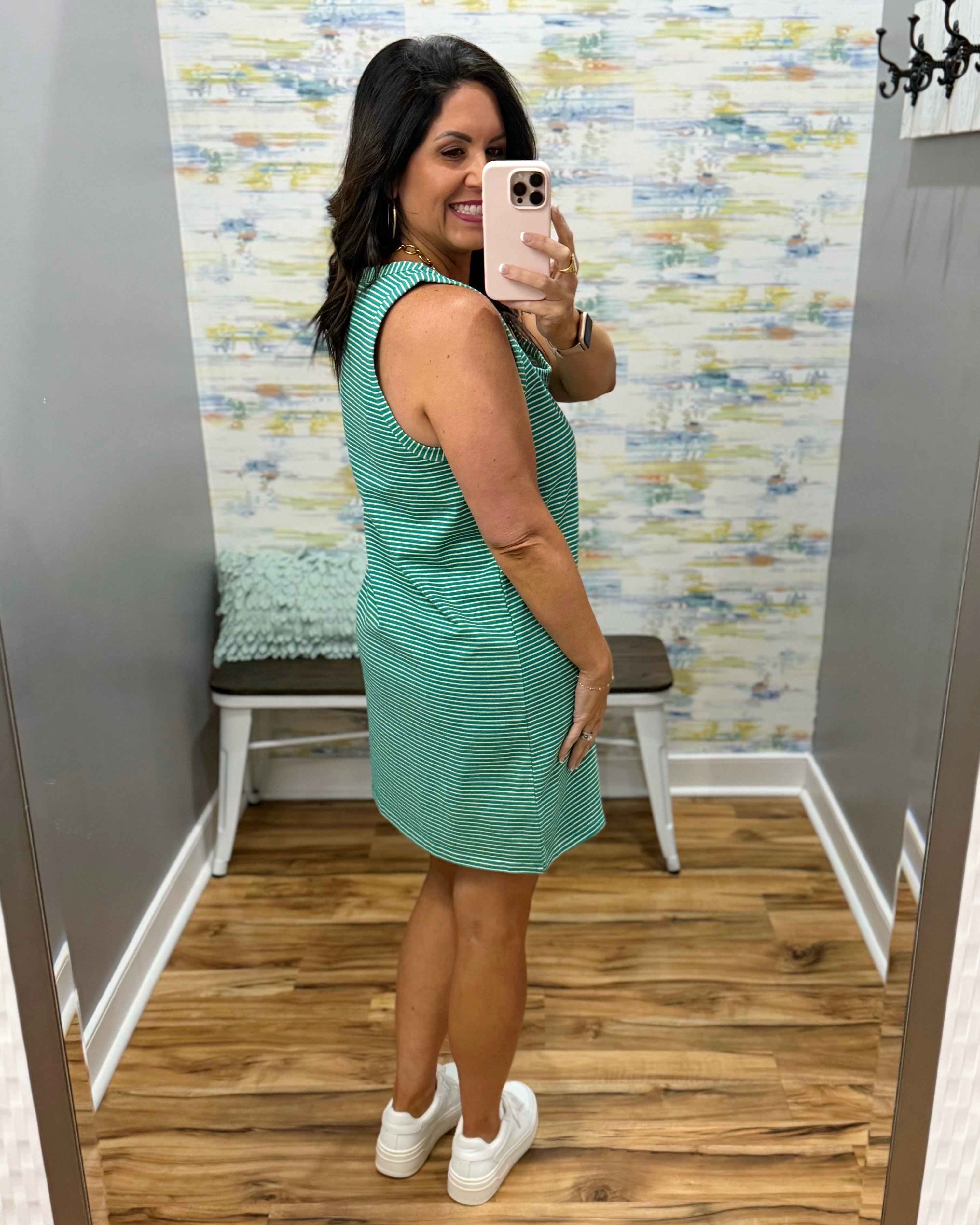 Woman taking a mirror selfie wearing a green dress in a fitting room.