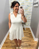 Woman taking a mirror selfie wearing a white dress in a room with wooden flooring and a colorful wall.