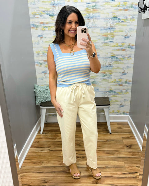 Woman wearing a striped top and beige pants in a room with a patterned wall.