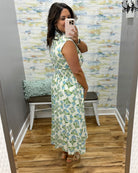 Woman taking a mirror selfie wearing a floral dress in a room with a textured wall.