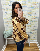woman wearing an abstract print long sleeve top in sand, taupe, and brown. 