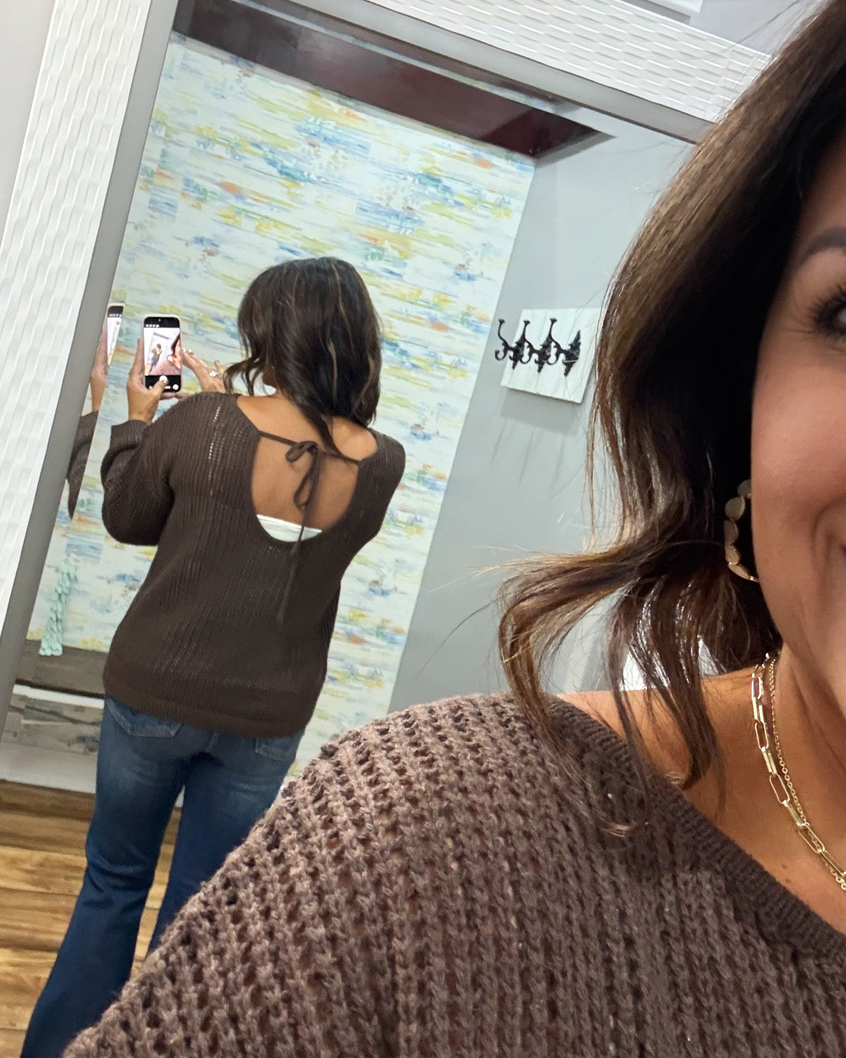 woman taking a selfie of the back of a brown crochet knit sweater showing the adjustable tie back feature.