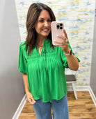 Woman taking a mirror selfie wearing a green blouse and blue jeans in a room with a colorful wall.