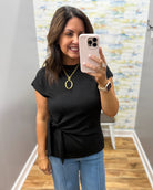 Woman taking a mirror selfie wearing a black top and blue jeans, holding a phone.