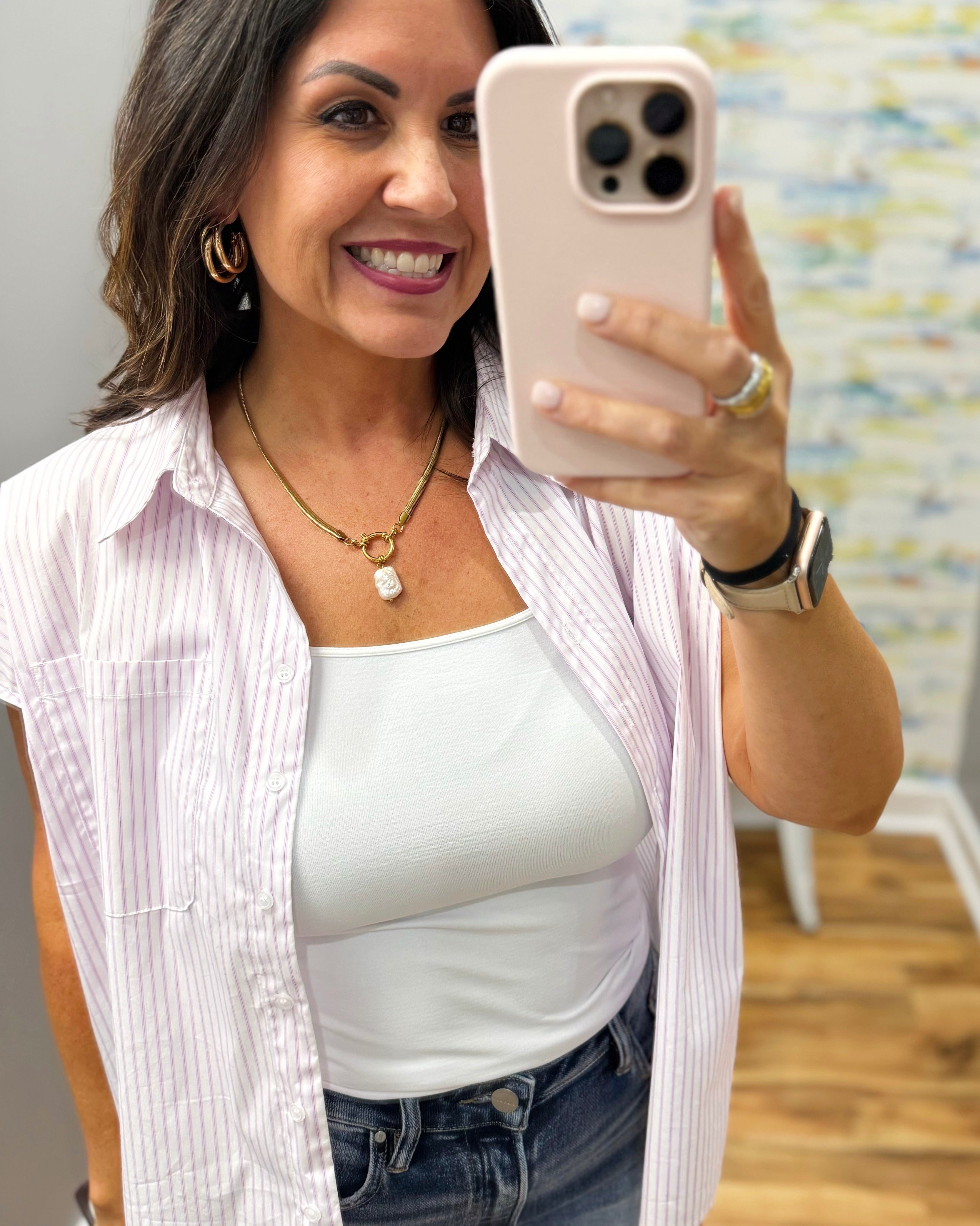 Woman taking a mirror selfie wearing a white top and striped shirt.