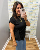 Woman taking a mirror selfie wearing a black top and blue jeans in a room with a colorful wall.
