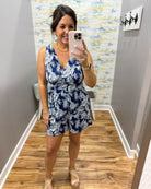 Woman taking a mirror selfie wearing a blue and white patterned romper in a room with wooden flooring and a colorful wall.