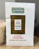 A packaged cross stitch kit labeled 'subversive cross stitch' with the design text 'FUCK CANCER' inside a framed preview, and 'FUCK CANCER CROSS STITCH KIT' printed below on a white package.