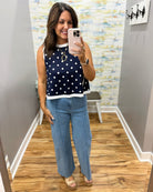 Woman taking a mirror selfie wearing a navy polka dot top and blue jeans in a room with a textured wall.