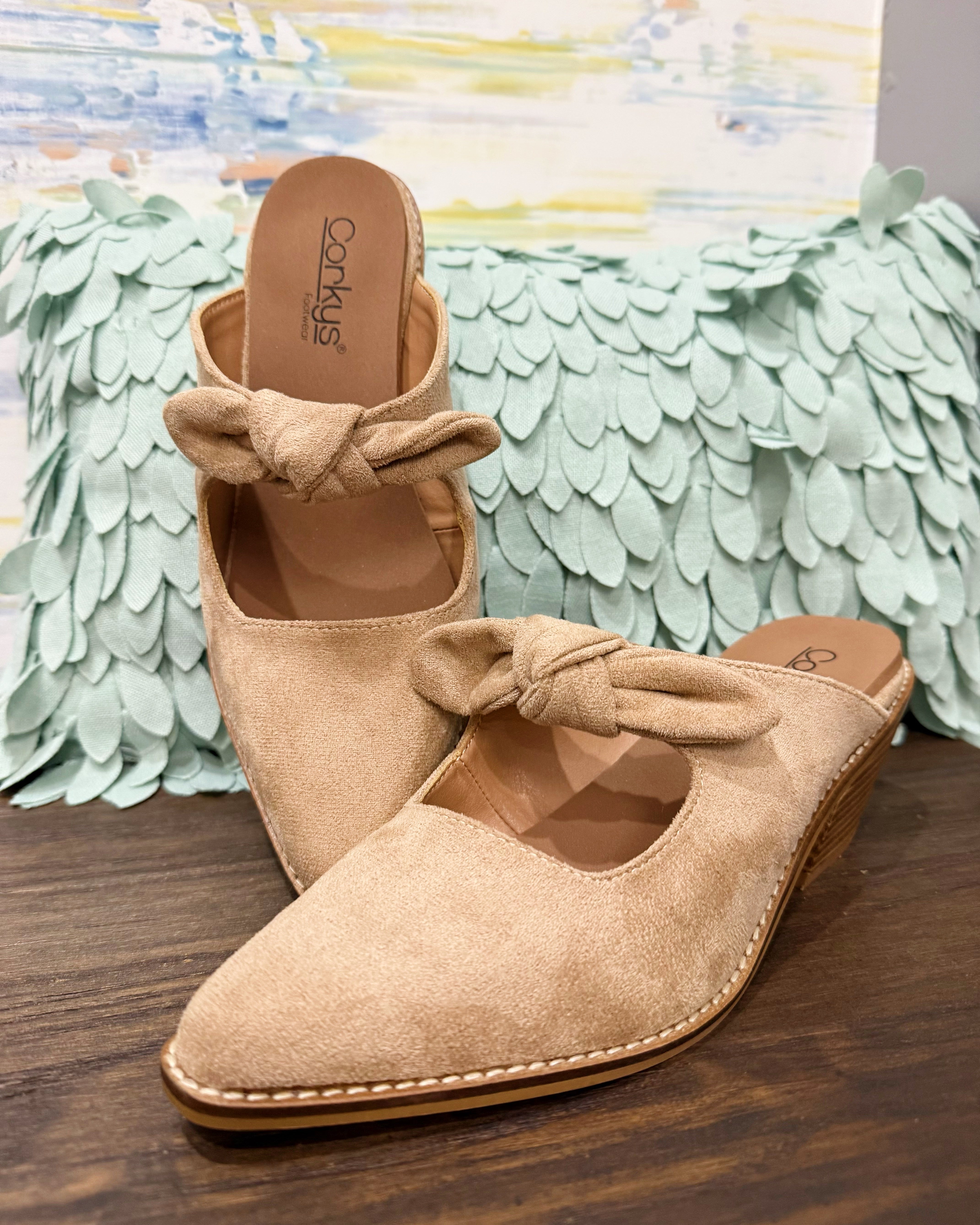 Corkys Oh Bow She Didn't Mule in camel faux suede is a chic slip-on shoe featuring a 2.5" wood grain block hell and a playful knotted bow detail