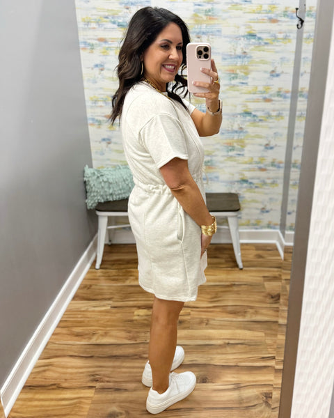 Woman wearing a neutral dress and white sneakers.