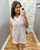 Woman taking a mirror selfie wearing a striped dress in a room with patterned wallpaper.