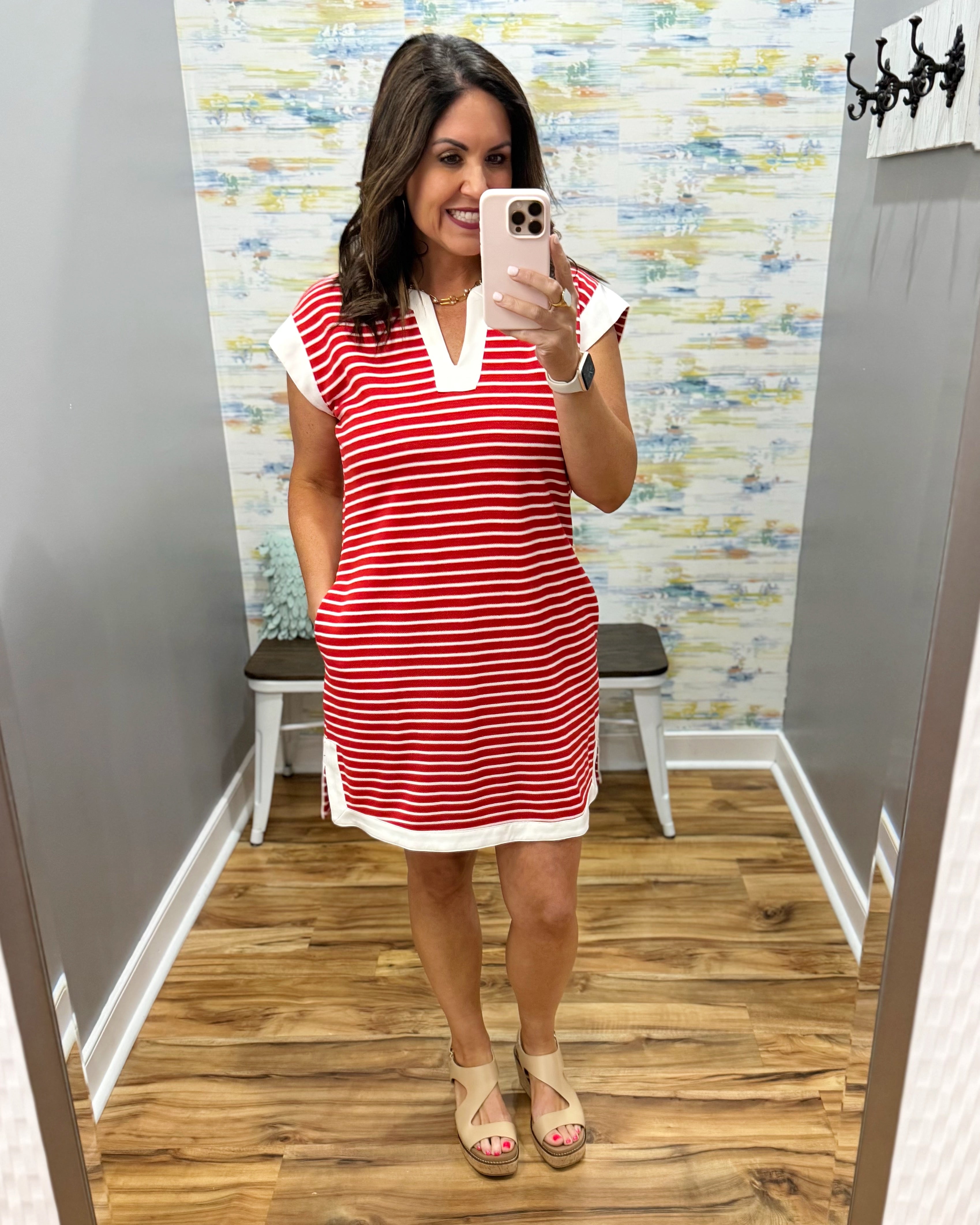 Woman taking a mirror selfie wearing a red and white striped dress in a fitting room.