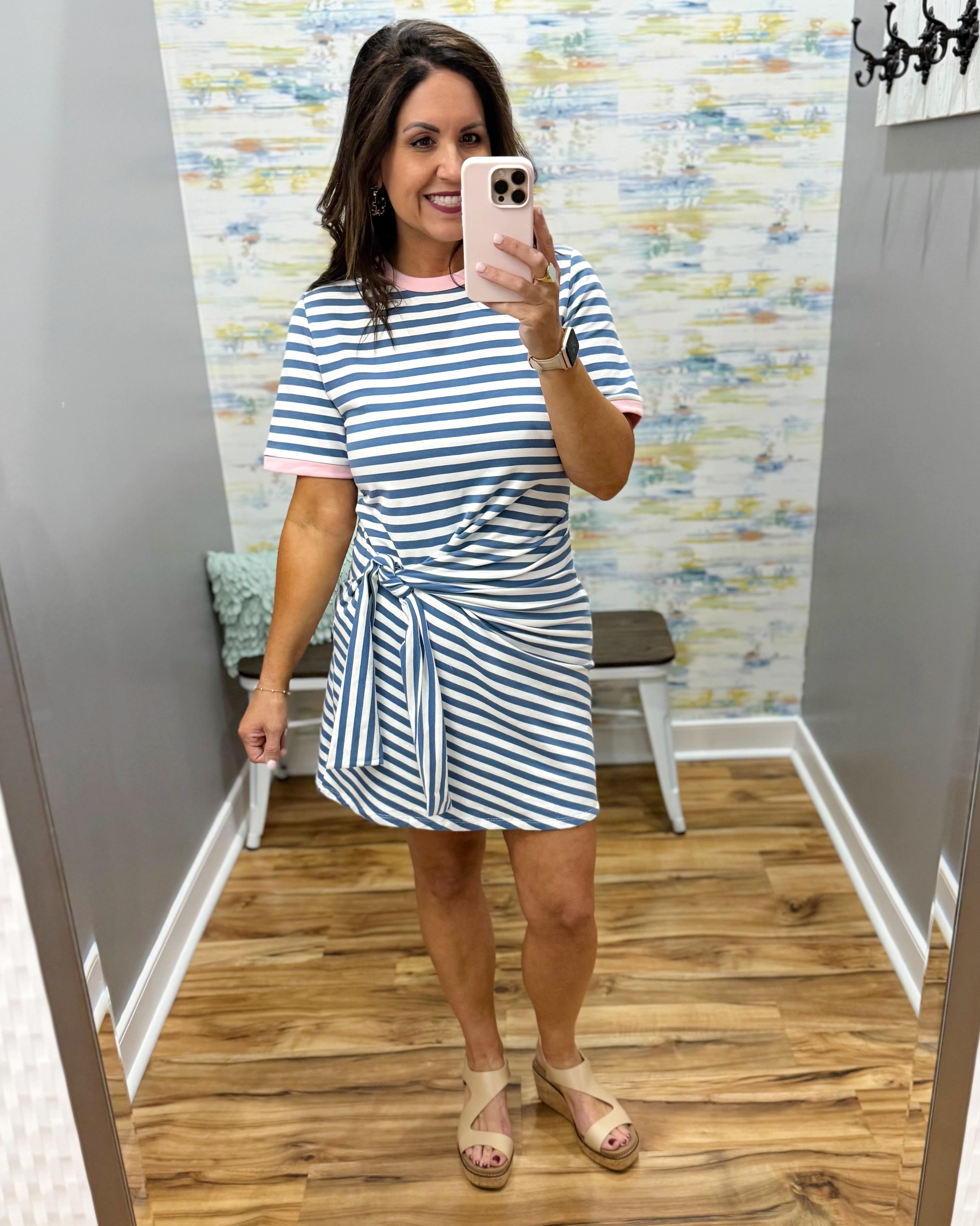 Woman taking a mirror selfie wearing a striped dress in a room with a patterned wall.