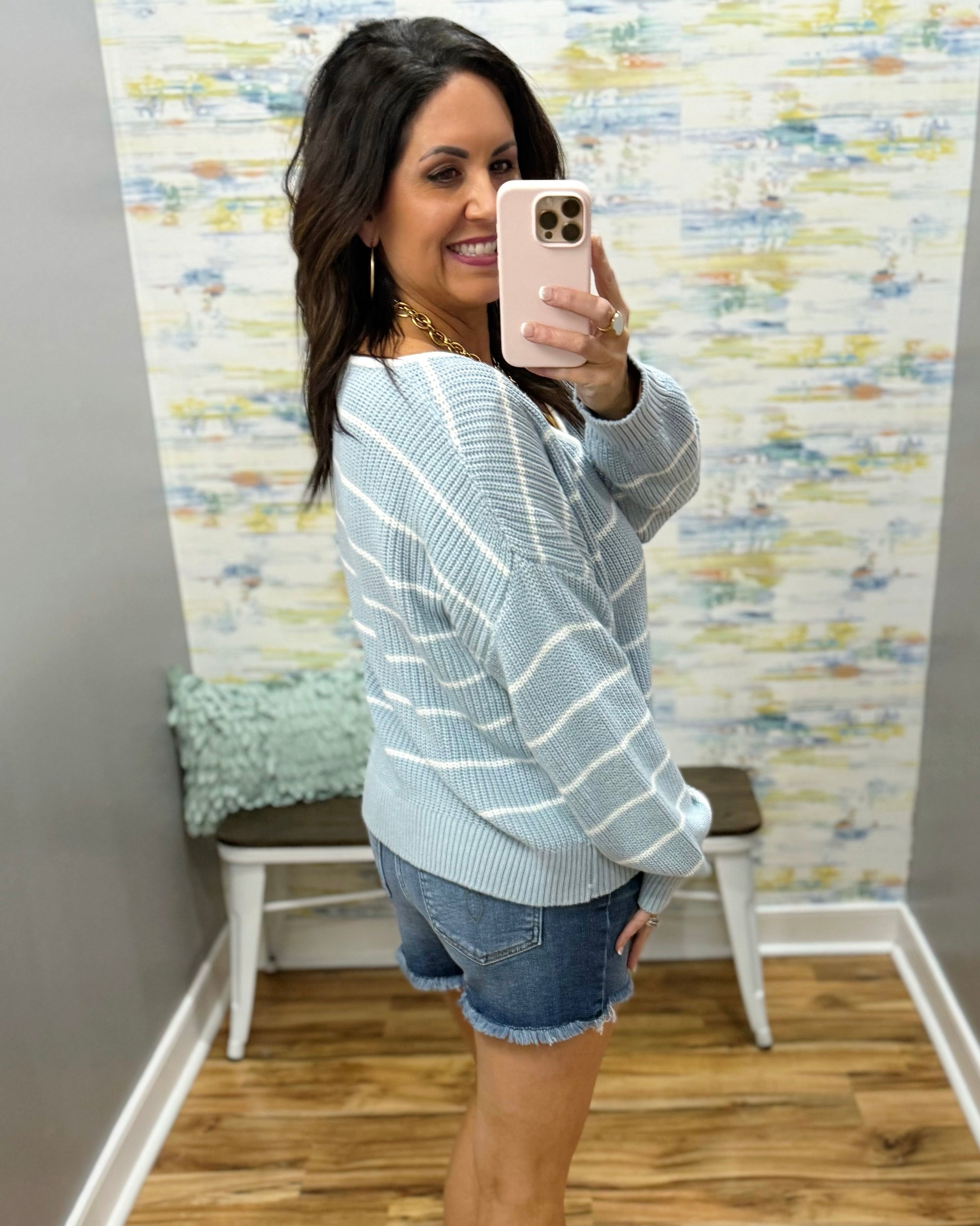Woman wearing a striped sweater and denim shorts in a room with a textured wall.