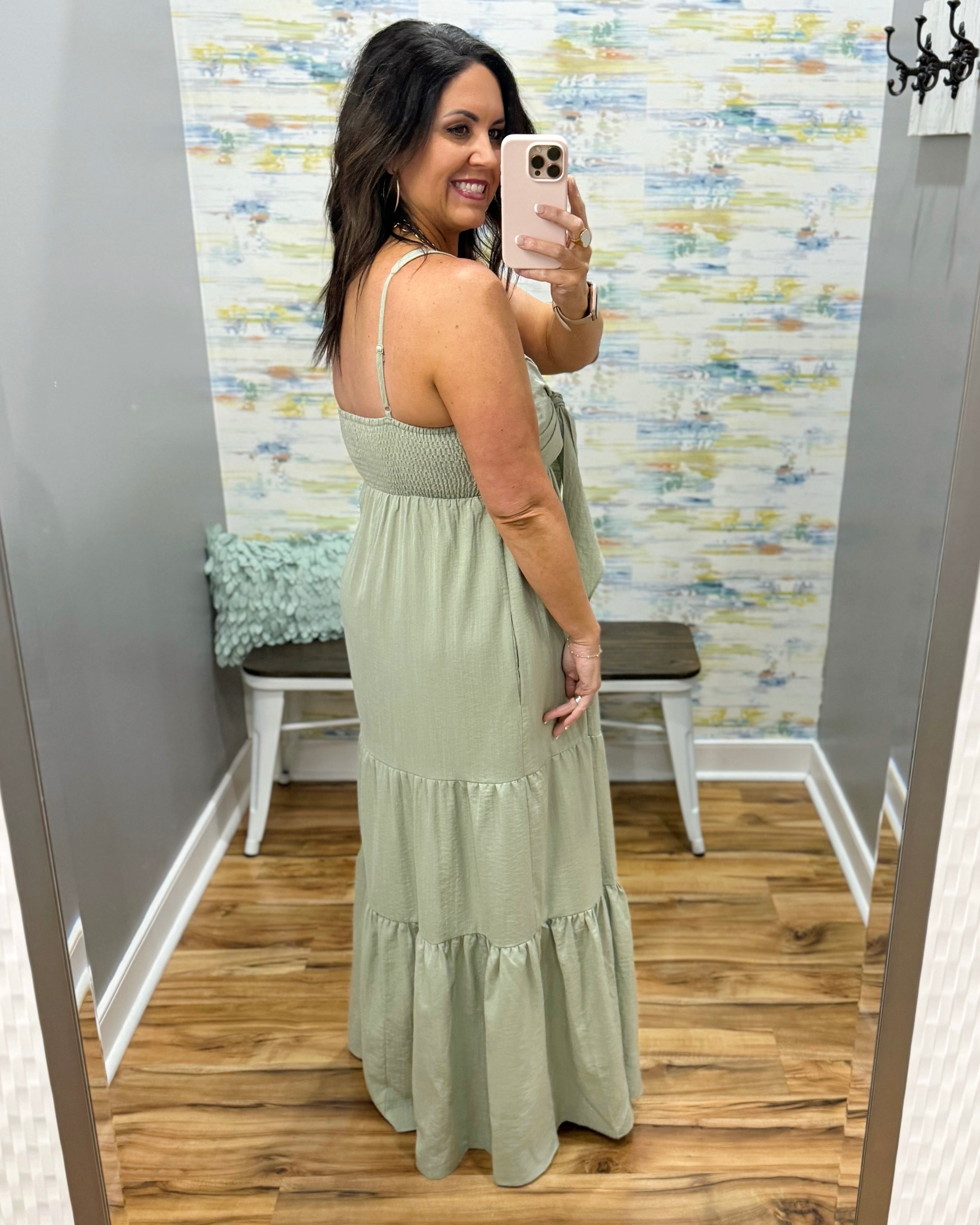 Woman wearing a long green dress in a room with patterned wallpaper.