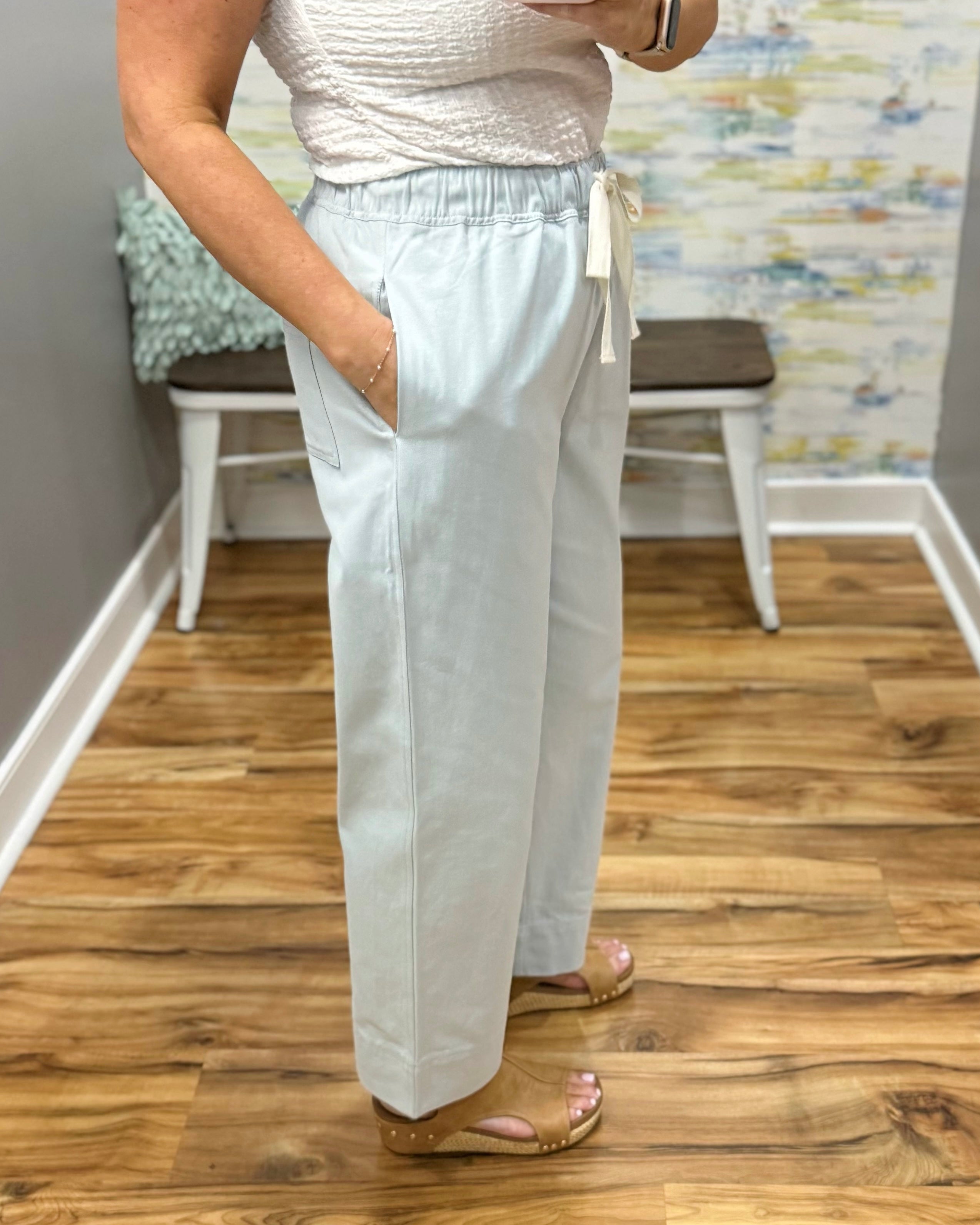 Person wearing light denim pants standing on a wooden floor with a colorful wall in the background.