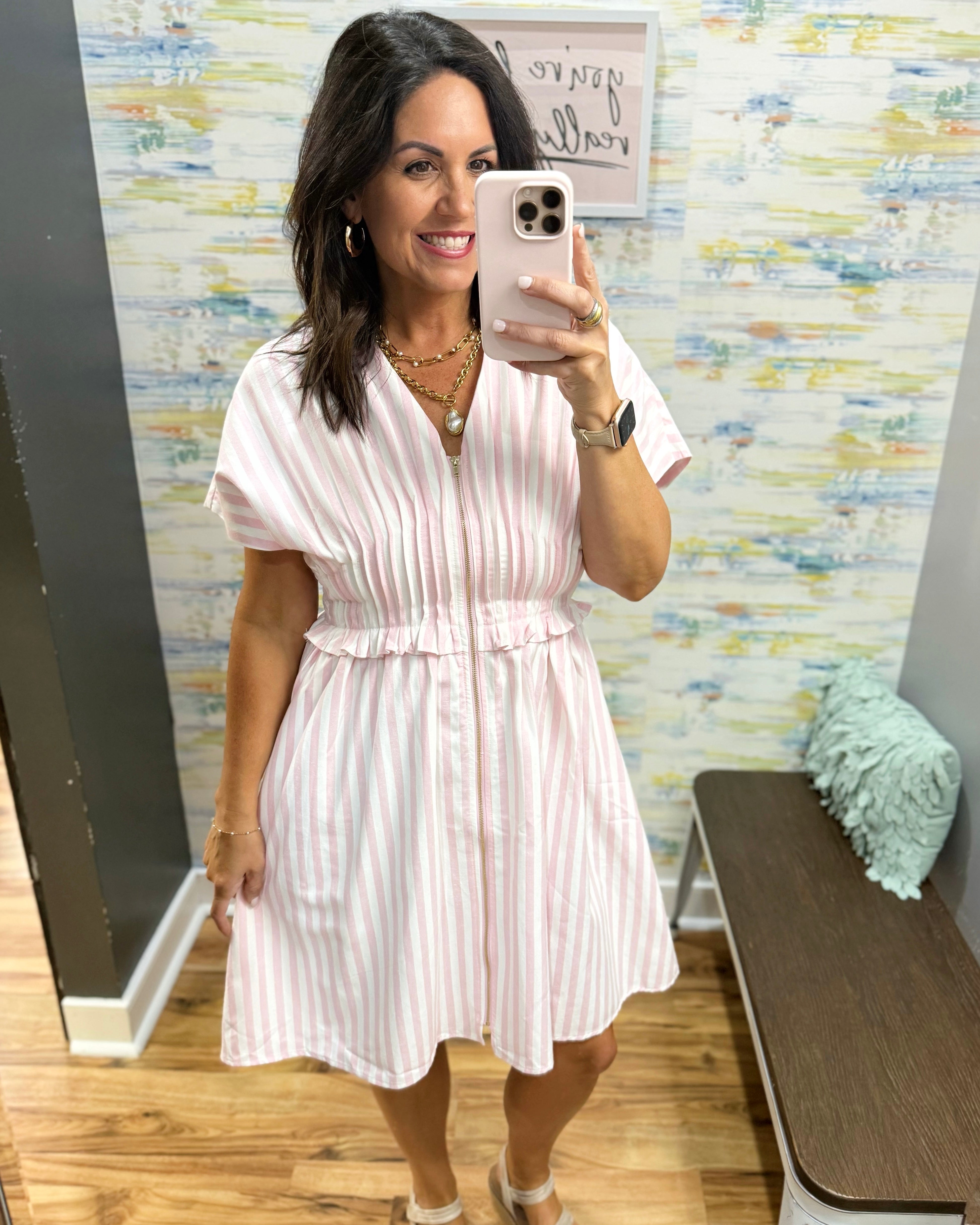 Woman taking a mirror selfie wearing a white dress in a room with colorful wall art.