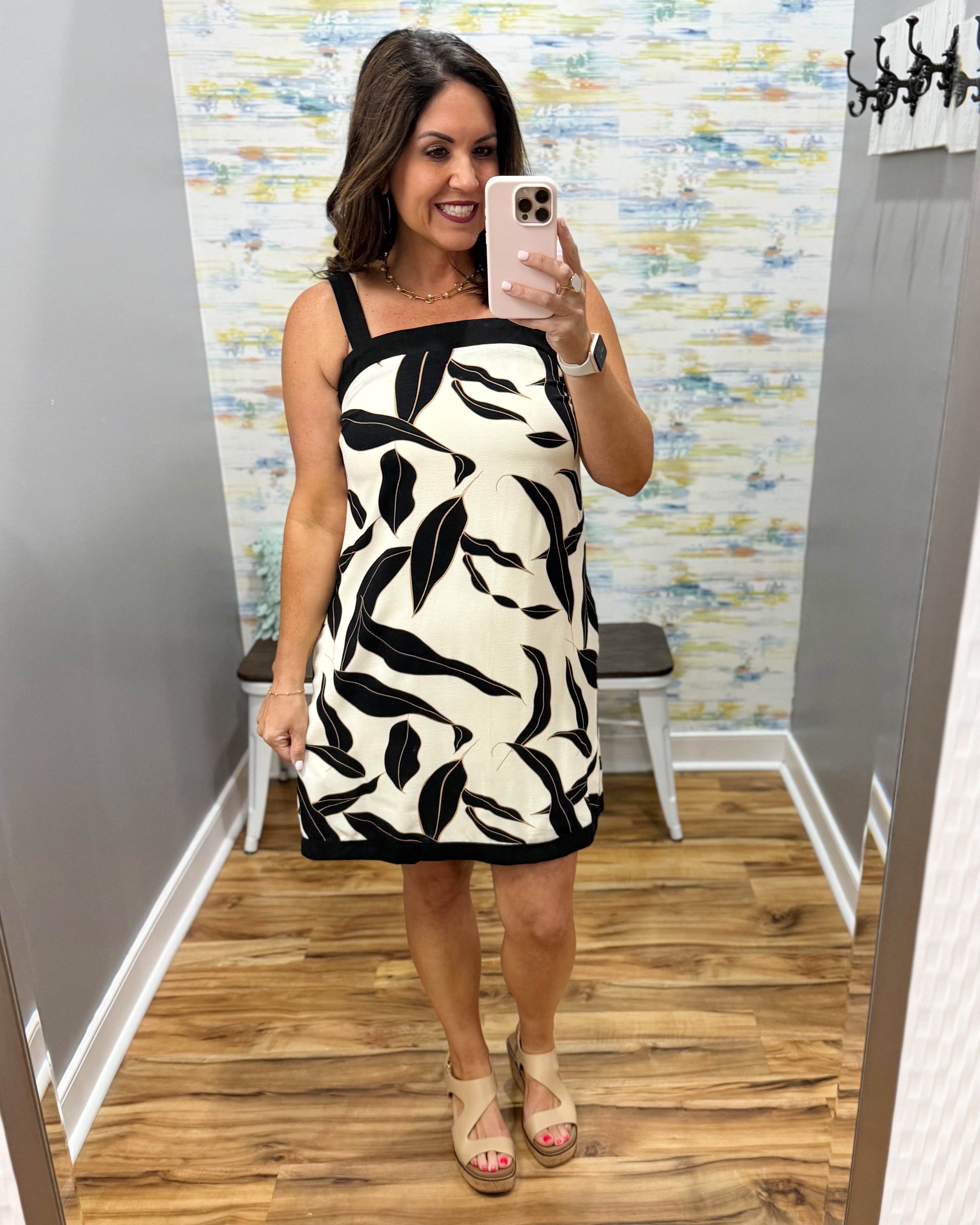 Woman taking a mirror selfie wearing a black and white patterned dress in a store.