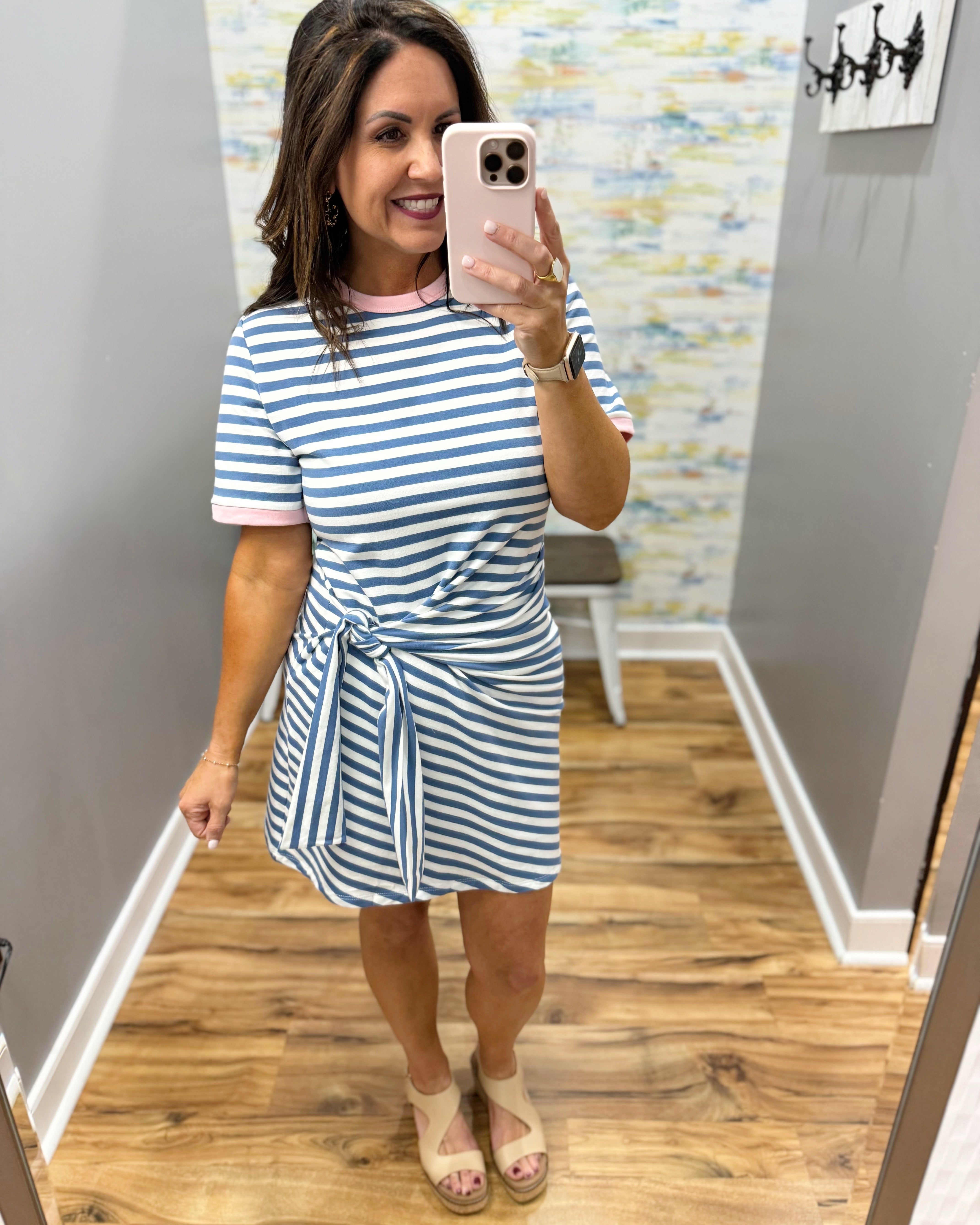 Woman taking a mirror selfie wearing a blue and white striped dress in a room with a patterned wall.