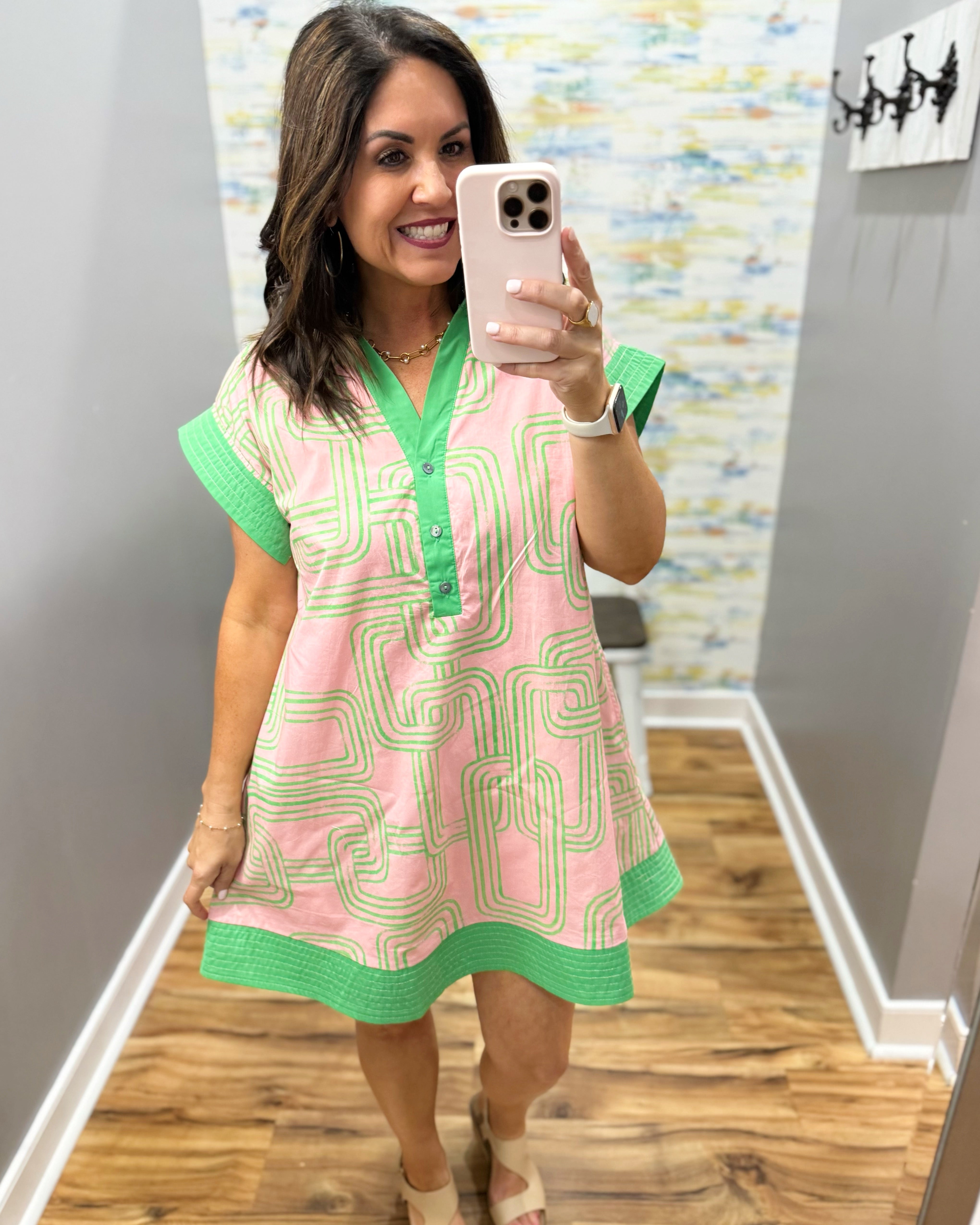Woman taking a mirror selfie wearing a pink dress with green accents in a room.