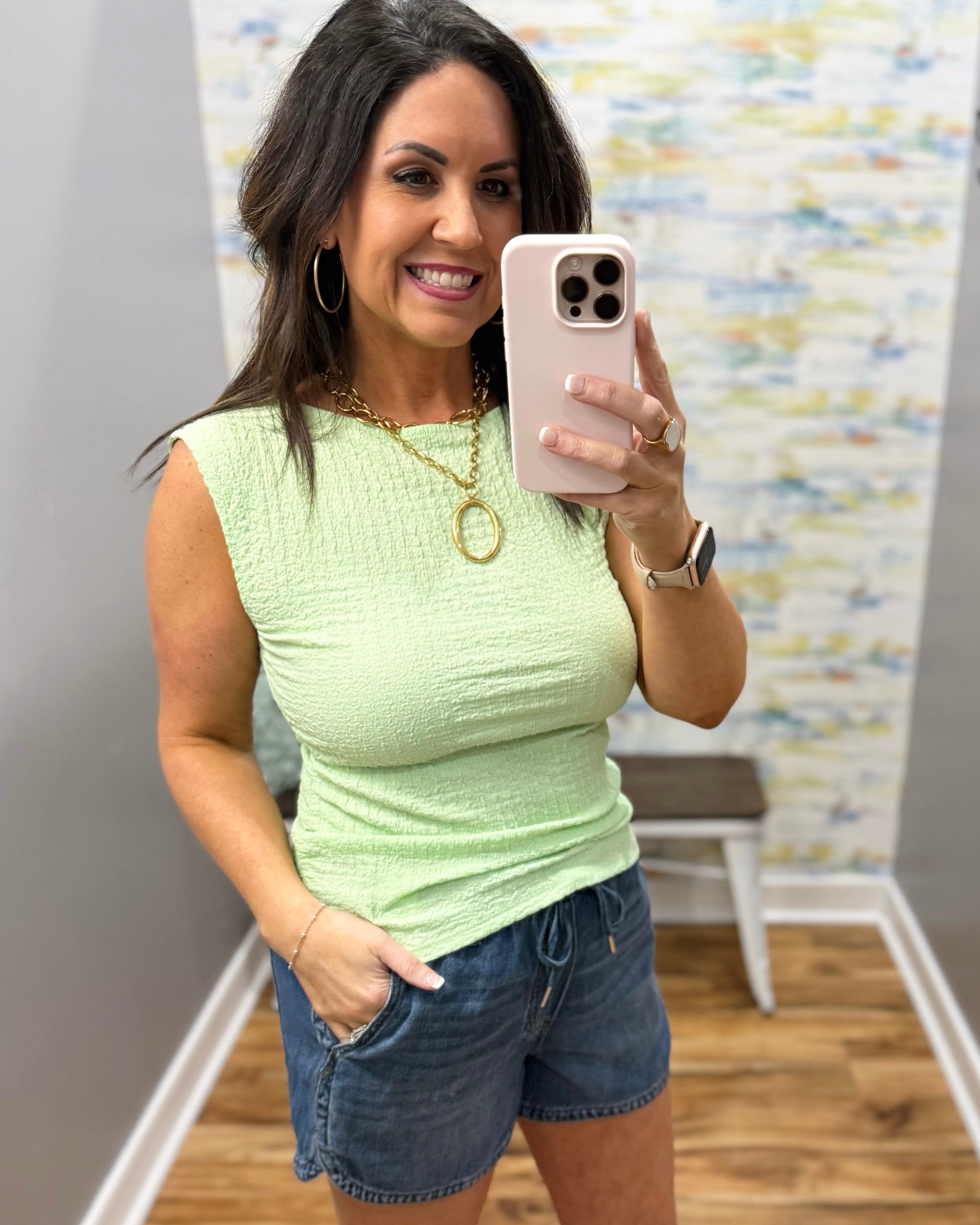 Woman wearing a light green top and denim shorts in a room with a colorful wall.