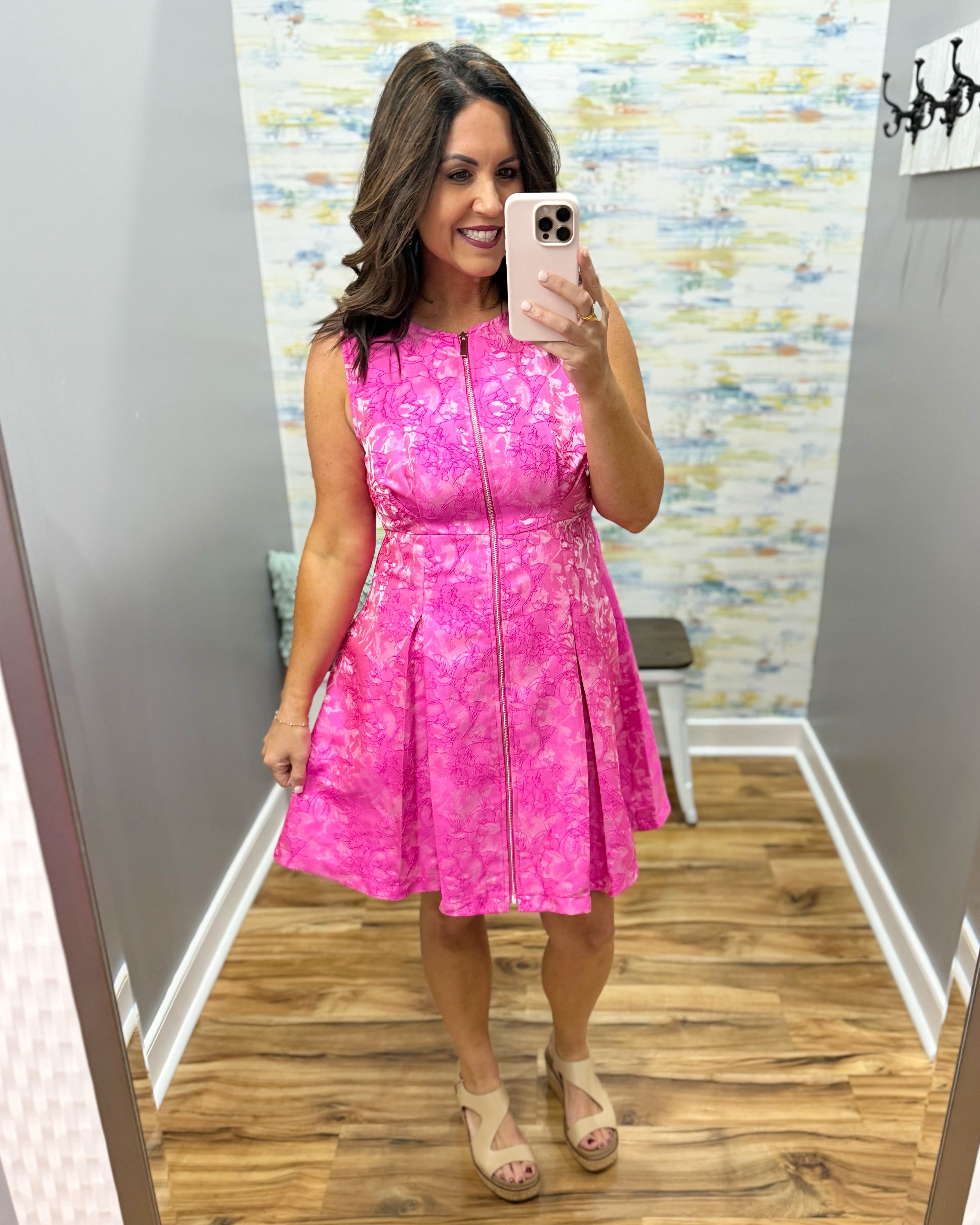Woman wearing a pink dress taking a mirror selfie in a store.