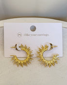 A pair of gold crescent-shaped hoop earrings with radiating sunburst spikes, displayed on a white card that reads 'i like your earrings.' with a small 'ps' logo.