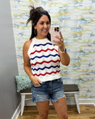 Woman taking a mirror selfie wearing a sleeveless top with red and blue stripes and denim shorts.