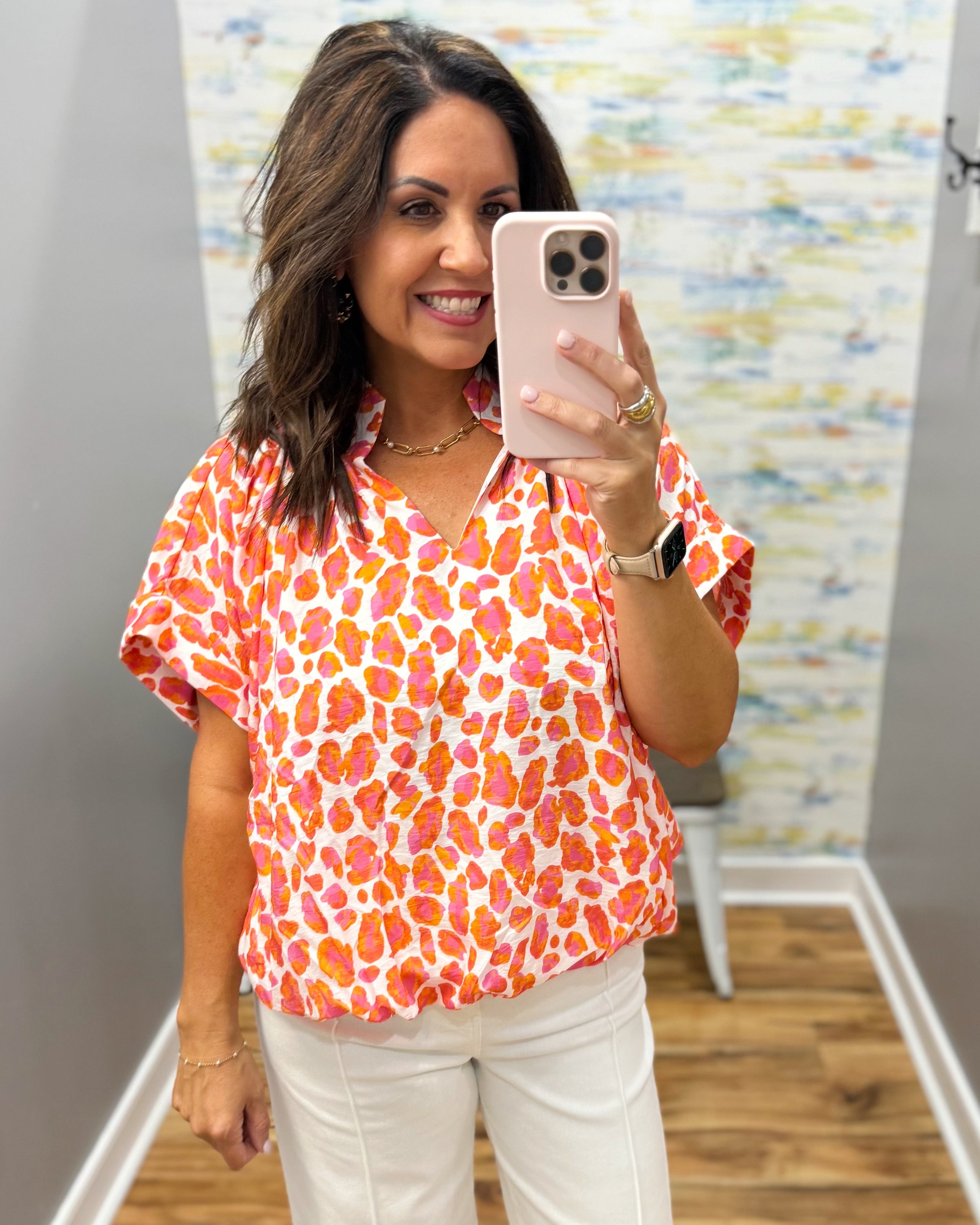 Woman taking a mirror selfie wearing an orange and pink patterned blouse.