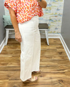 Person wearing a colorful top and white pants standing on a wooden floor.