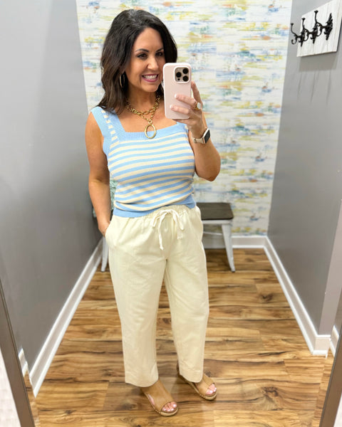 Woman wearing a striped tank top and light-colored pants in a room with a textured wall.