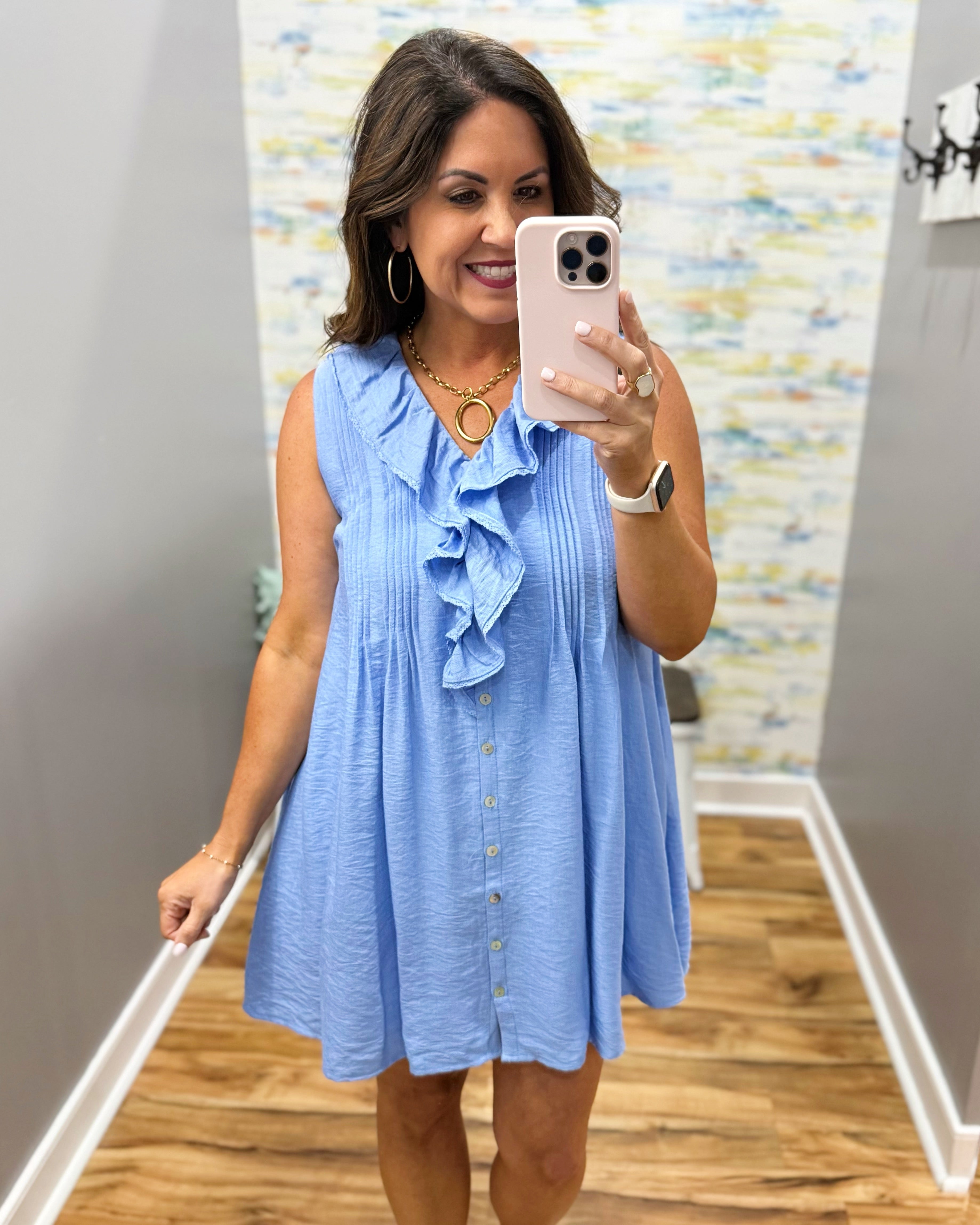 Woman taking a mirror selfie wearing a blue dress in a room with a colorful wall.