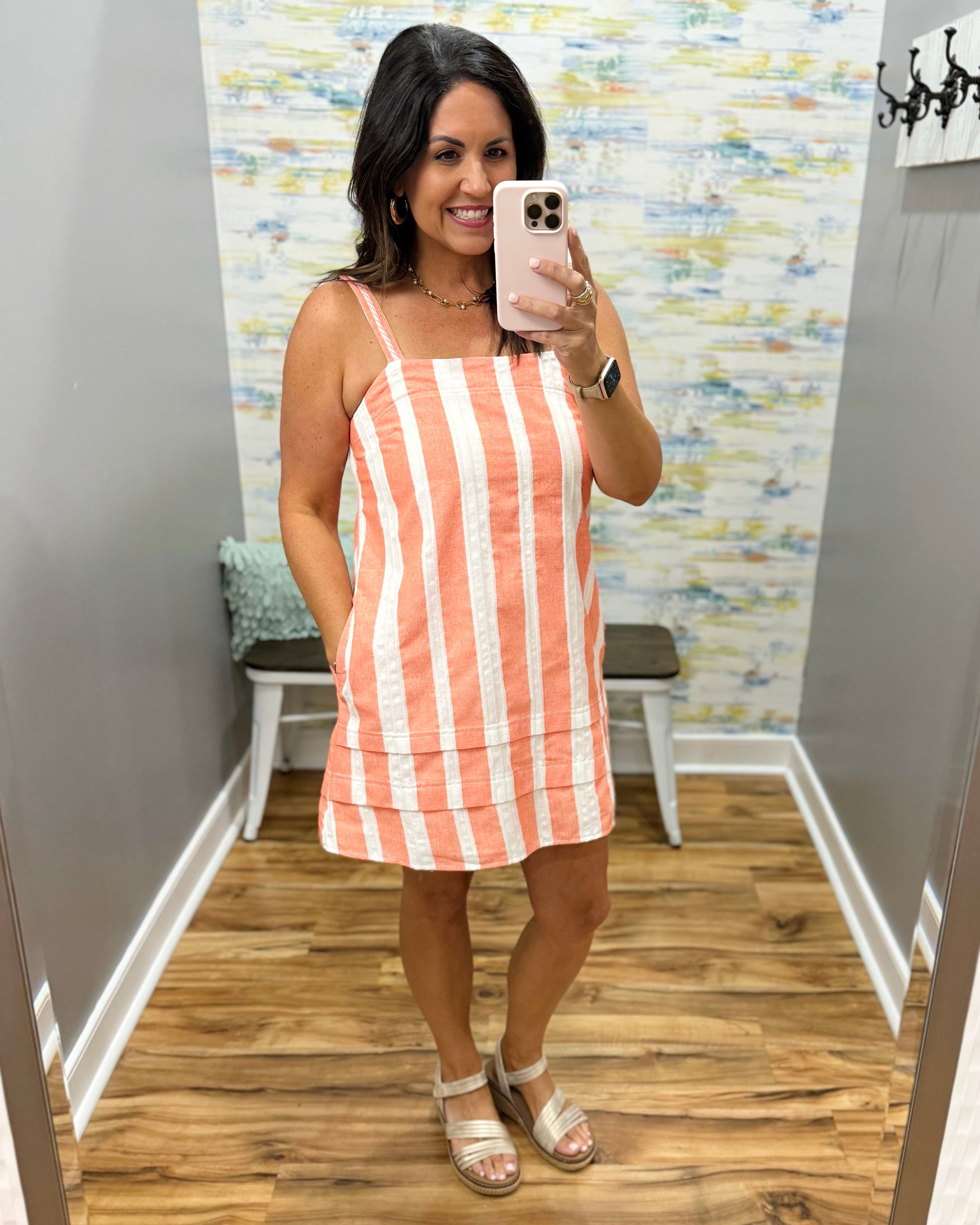 Woman taking a mirror selfie wearing a striped dress in a fitting room.