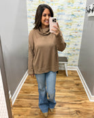 A woman takes a mirror selfie in a fitting room wearing a brown cowl-neck knit top and blue flare jeans.