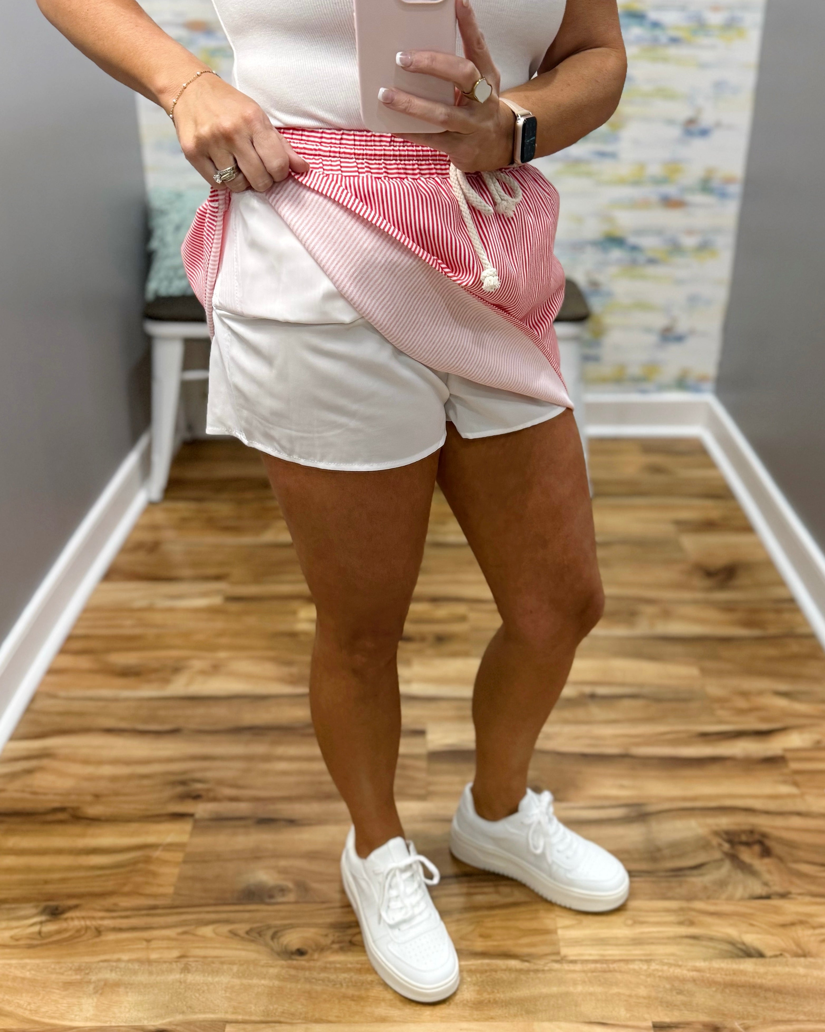 Person wearing a white top, pink drawstring bag, and white shorts on a wooden floor.