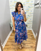 Woman taking a mirror selfie wearing a blue floral dress in a room with a patterned wall.