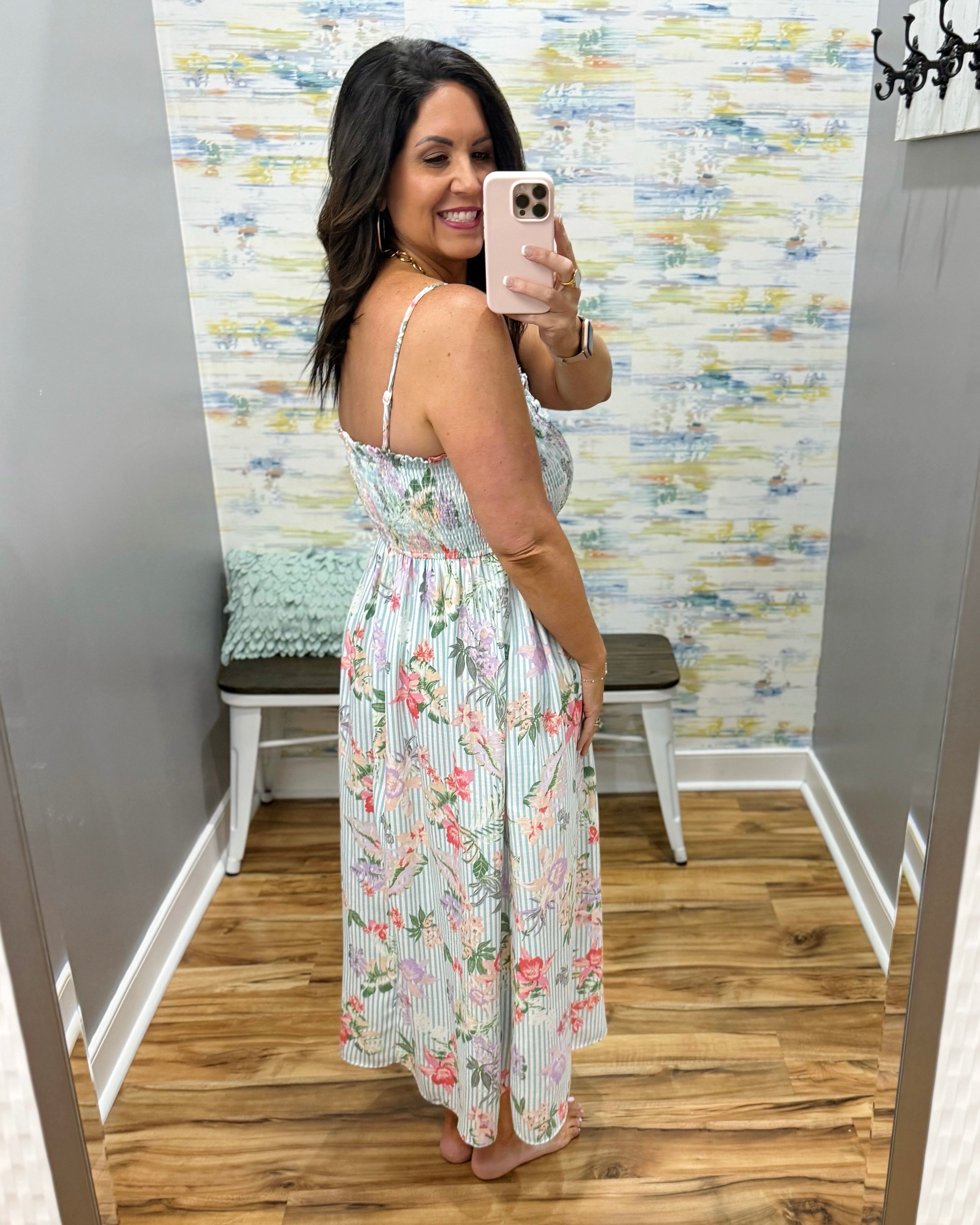 Woman taking a mirror selfie wearing a floral dress in a room with a colorful wall.