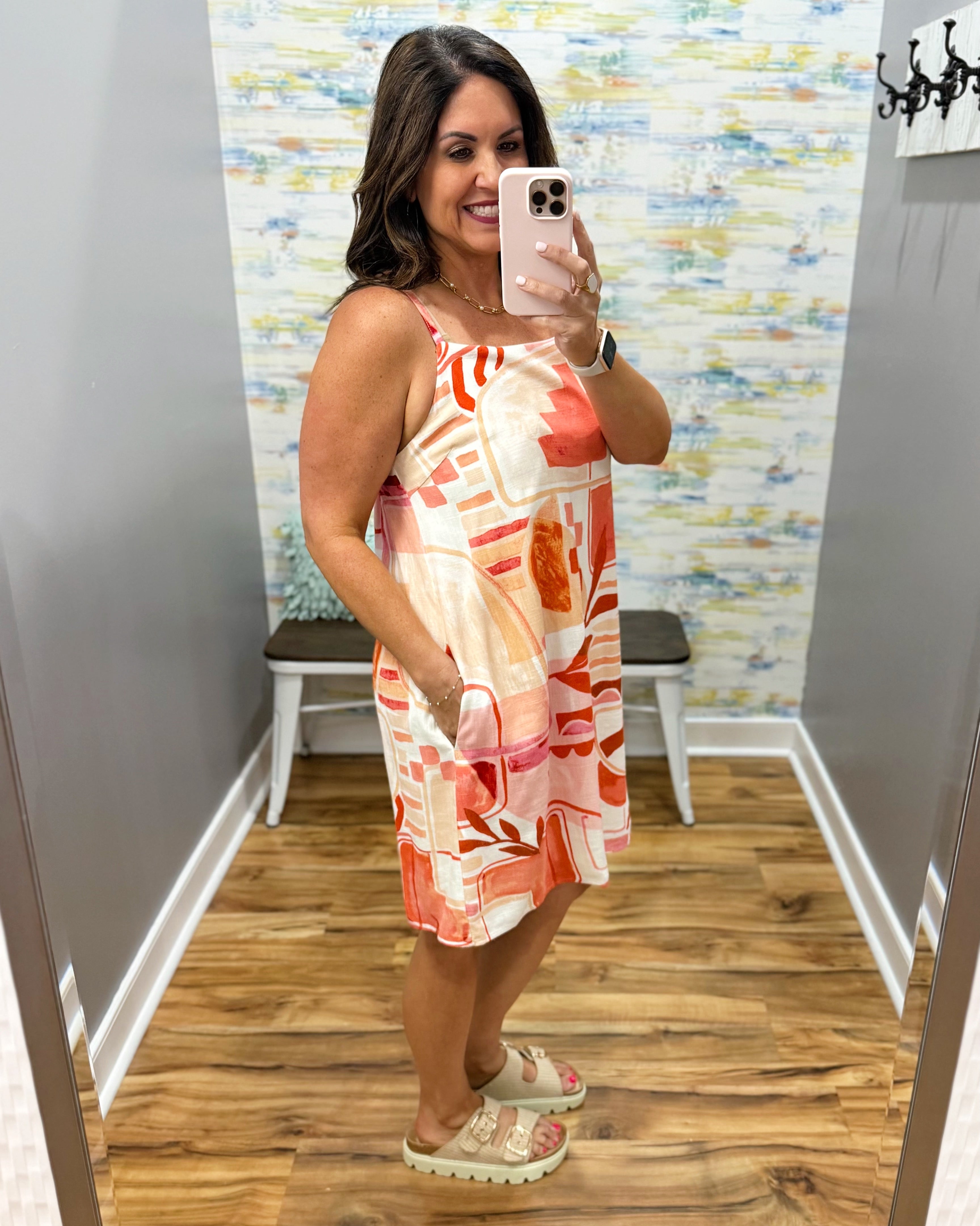 Woman taking a mirror selfie wearing a patterned dress in a room with a colorful wall.