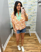 Woman taking a mirror selfie wearing a colorful blouse and denim shorts in a store.