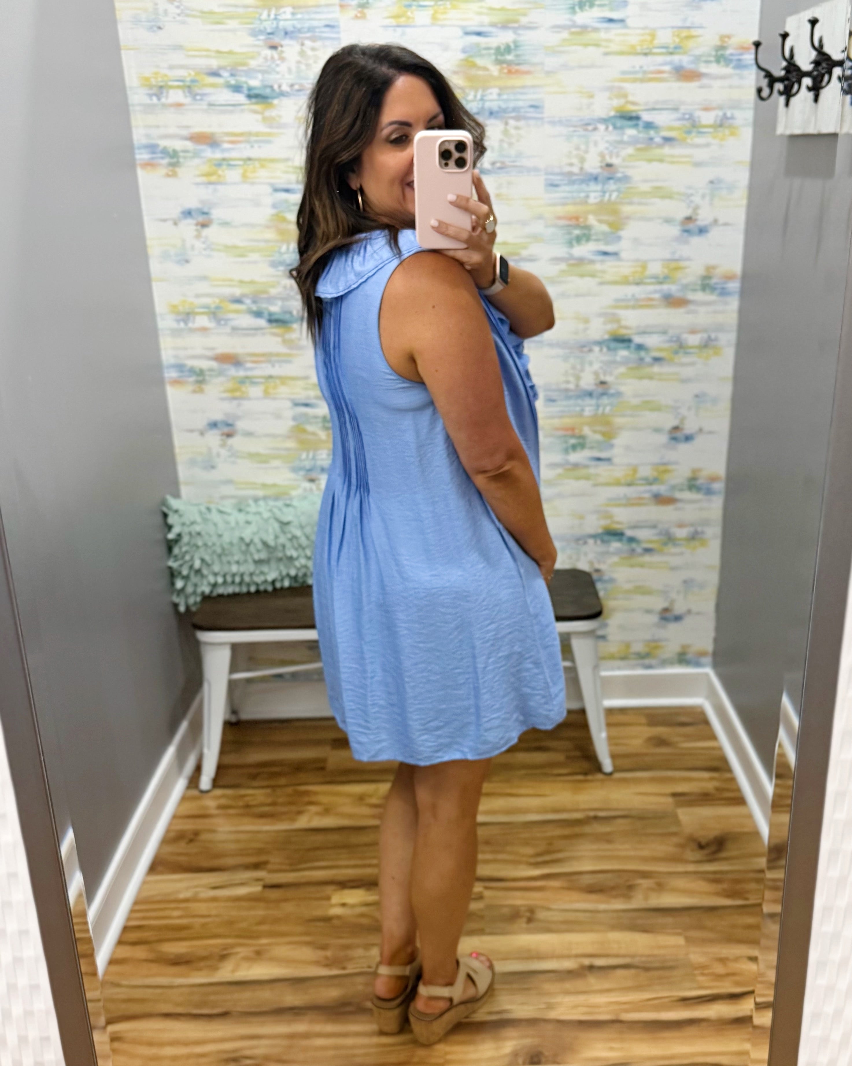 Woman taking a mirror selfie wearing a blue dress in a room with a colorful wall.
