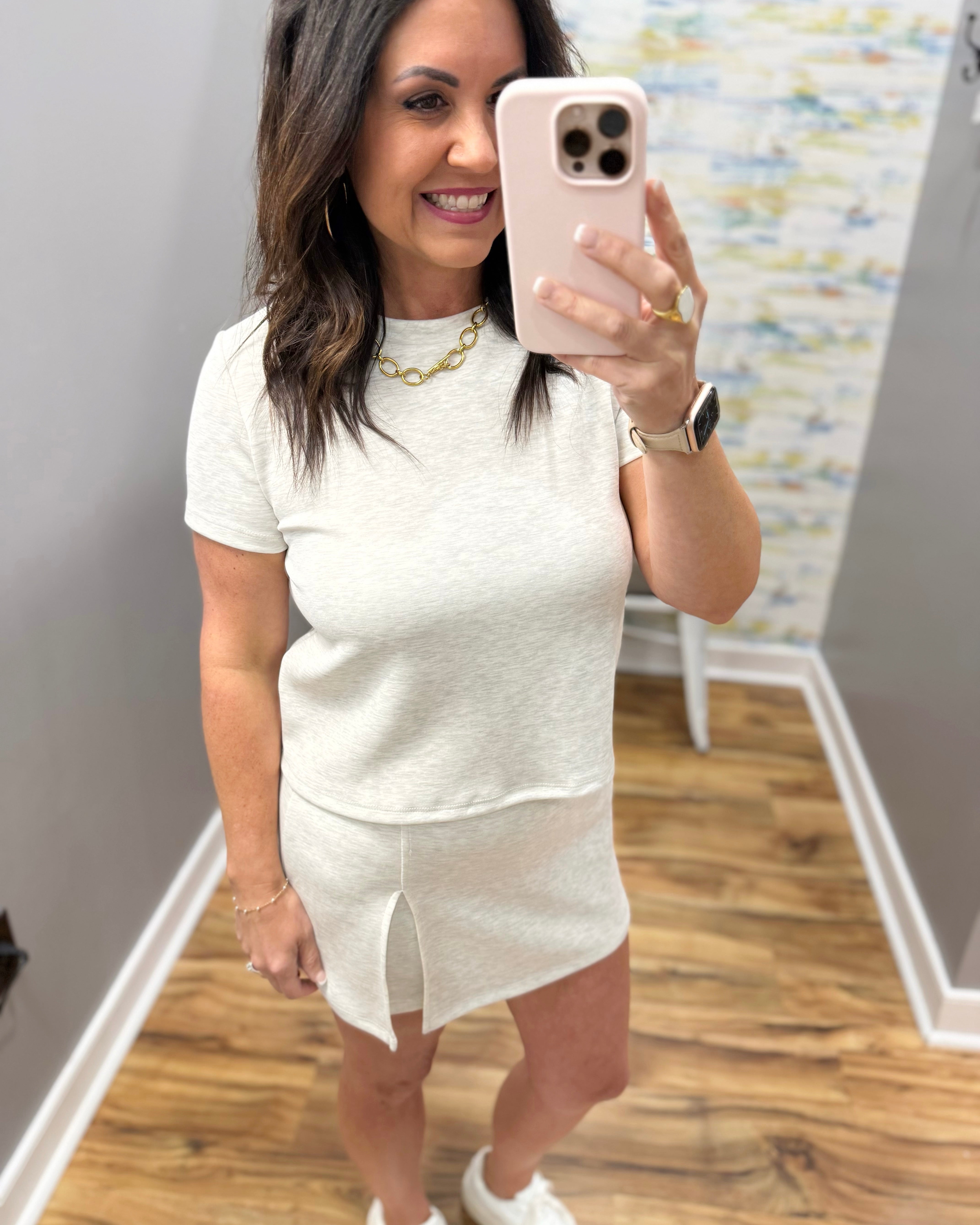 Woman taking a mirror selfie wearing a white dress in a room with a patterned wall.