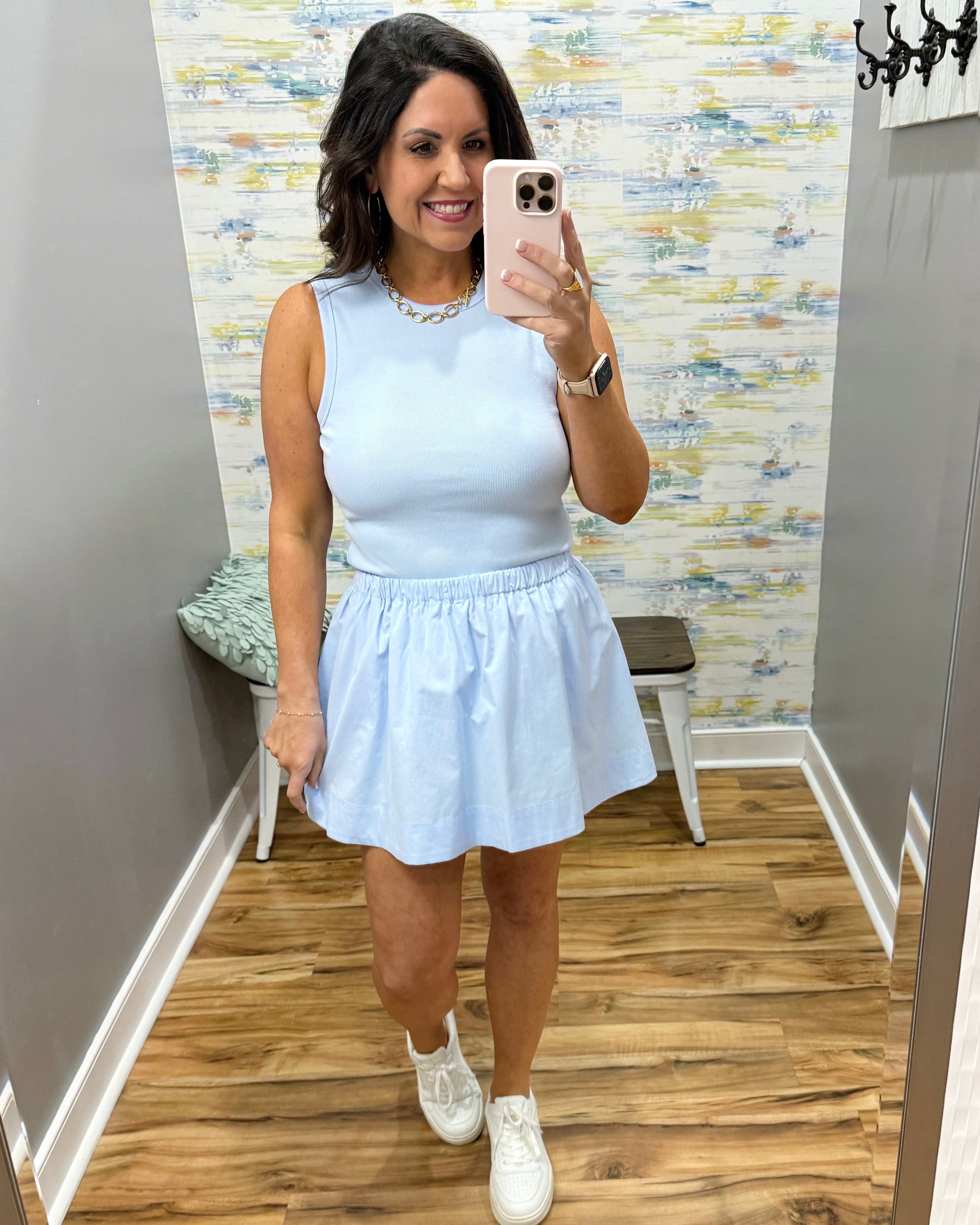 Woman taking a mirror selfie wearing a light blue dress in a room with patterned wallpaper.